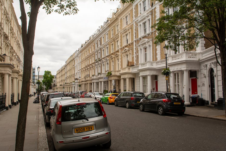 Two removal workers from South Kensington Man and Van are preparing for a home relocation outside a shop with a blue façade and gold signage that reads 'GUANG' in an urban area. The workers, dressed i
