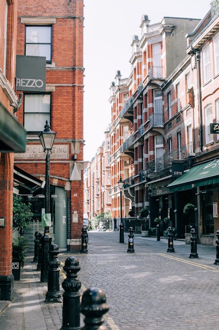 A narrow cobbled street in South Kensington lined with residential buildings on both sides. The left side features a row of quaint houses with white and pastel-colored facades, some with small balconi